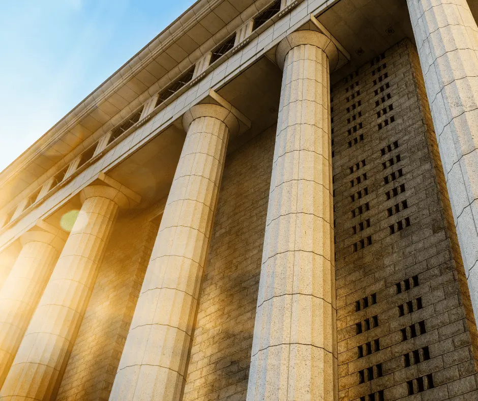 A courthouse featuring impressive columns, bathed in sunlight that casts a warm glow behind the structure.